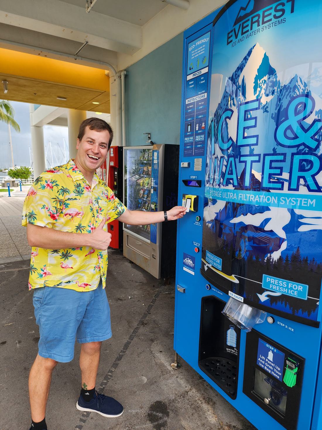 Alex Koon using a Pure Ice USA vending machine at a marina, with the machine in the background